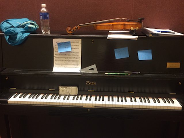 A violin resting on top of an upright piano in a lesson studio, with sheet music nearby.