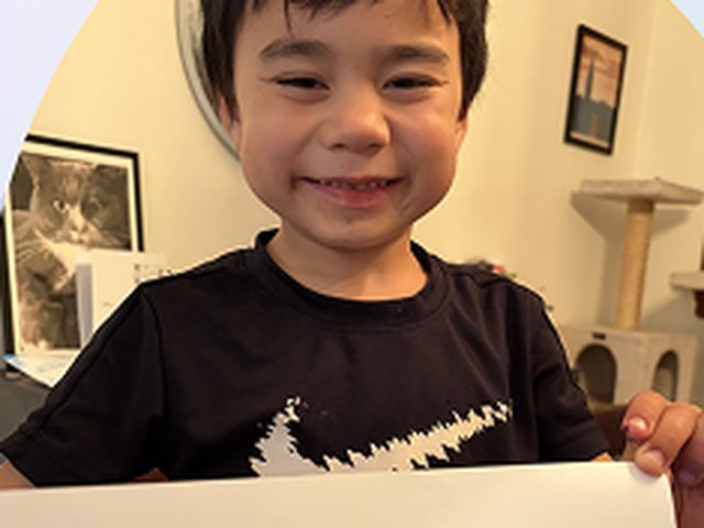 A smiling young boy holding up a hand-drawn picture of a violin.