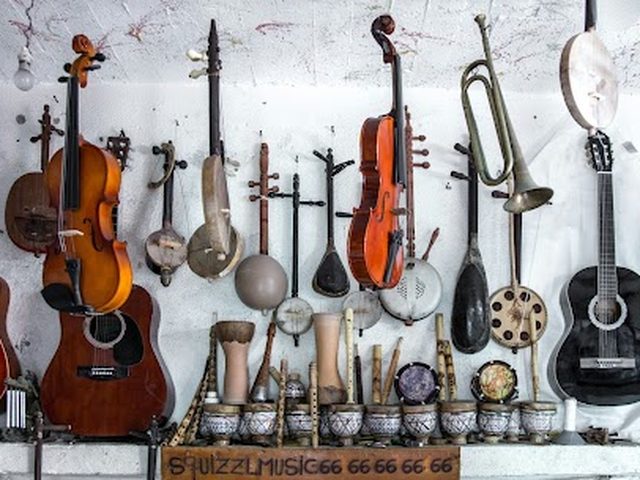 A wall of instruments on display, including violins, guitars, and a trumpet, at a music shop.