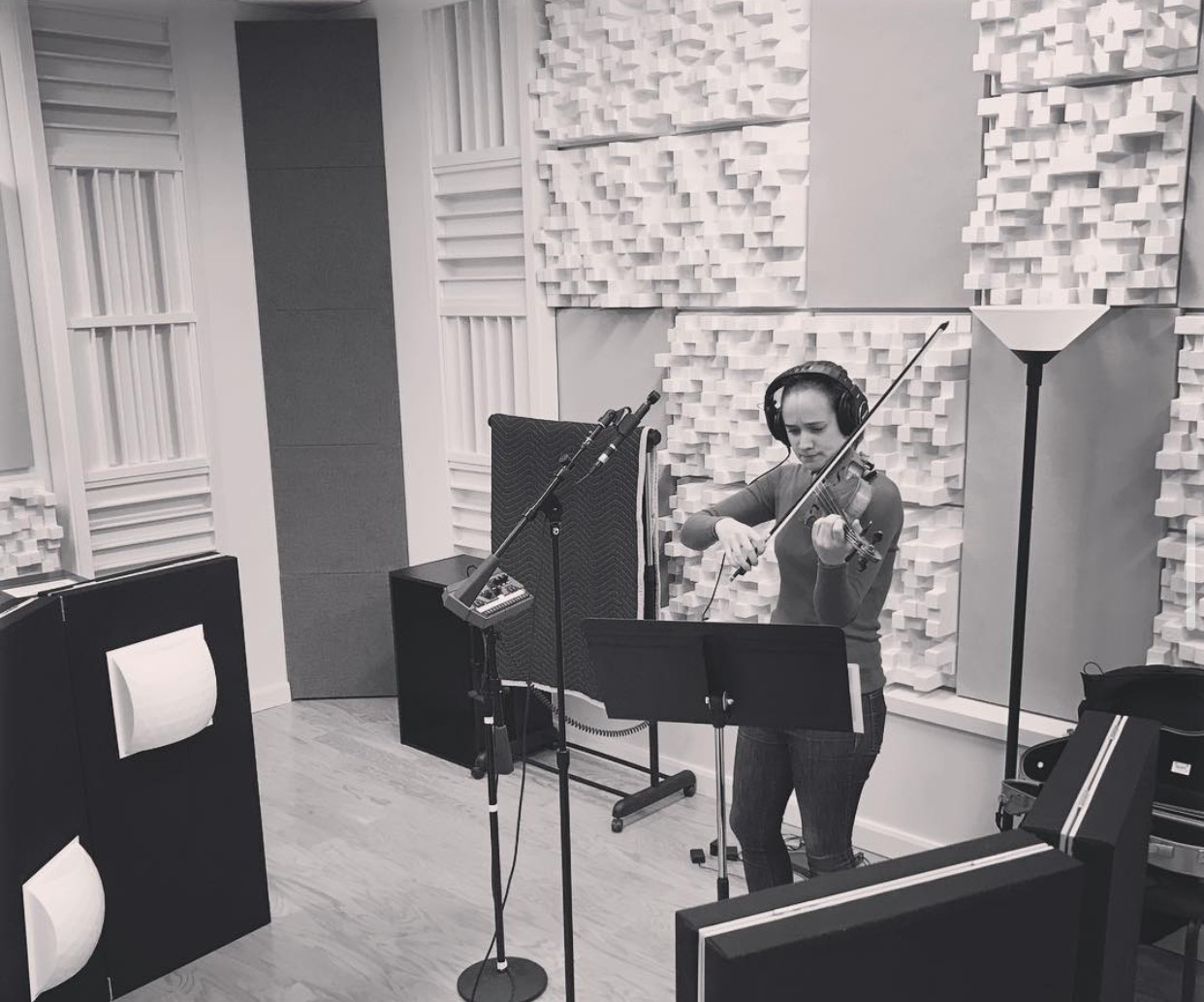 A violinist playing in a recording studio, surrounded by acoustic foam paneling, in black and white.